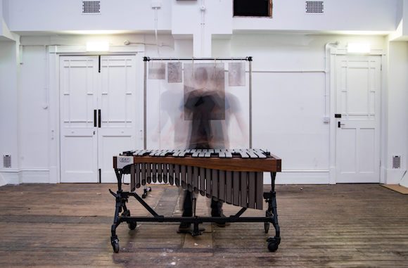 Alex Petcu at a vibraphone, blurred in motion, in a bright empty room